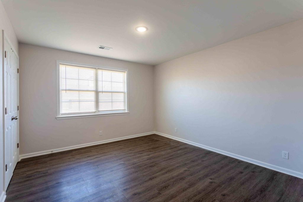 a bedroom with white walls and wood floors and a window