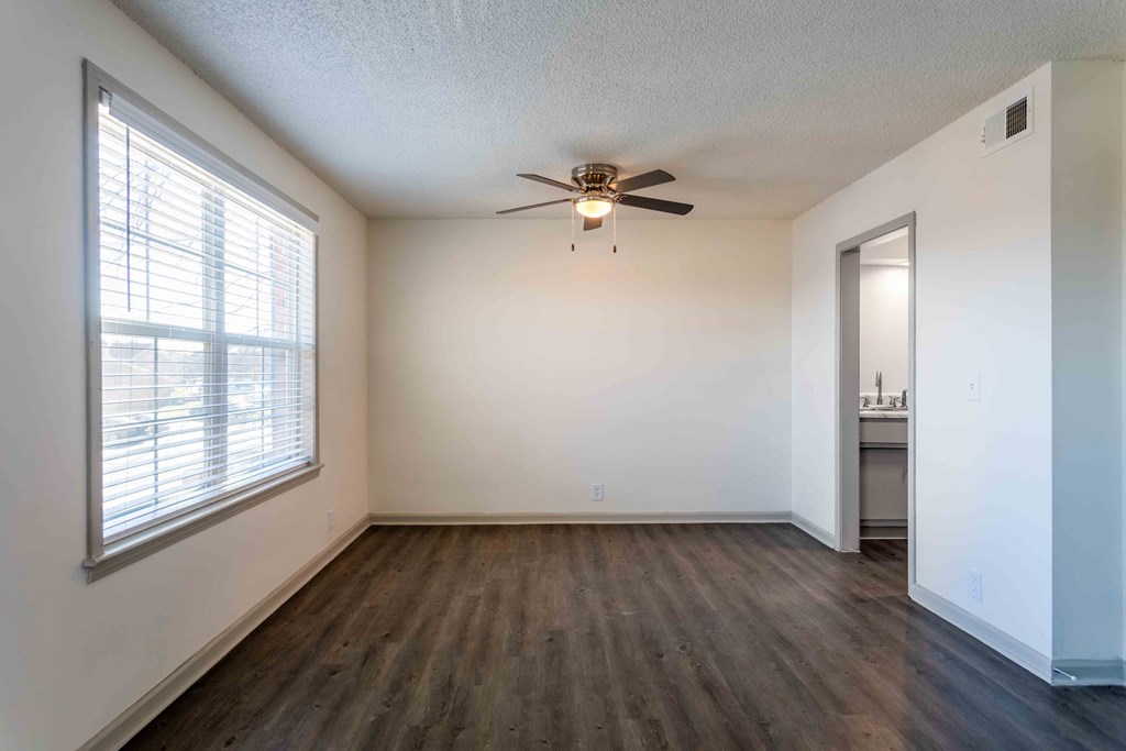 an empty living room with a large window and a ceiling fan
