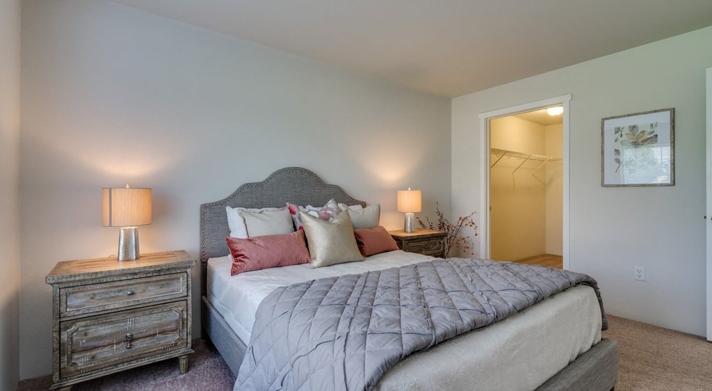 Apartments For Rent In Coeur d'Alene, ID - Rockwood Lodge - Bedroom With Carpeted Flooring, Large Bed, Wooden Nightstands With Lamps, And Spacious Closet.