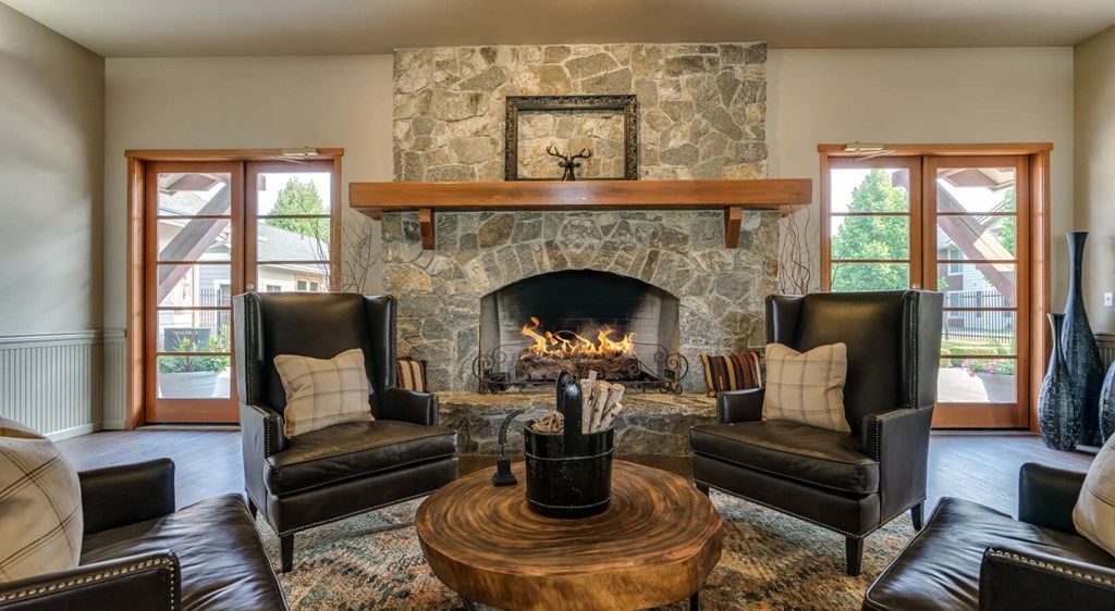 Apartments In Coeur d'Alene, ID - Rockwood Lodge - Resident Clubroom With Wood-Style Flooring, Area Rug, Leather Armchairs, Coffee Table, And Fireplace.