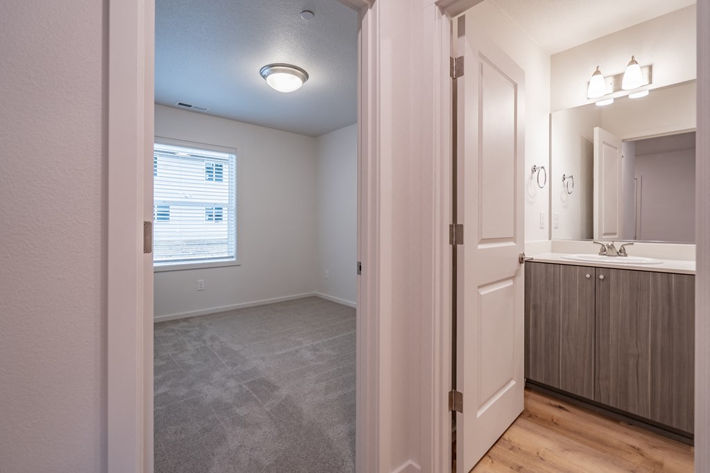 a bedroom with a medium sized window and a bathroom with a sink and a mirror
