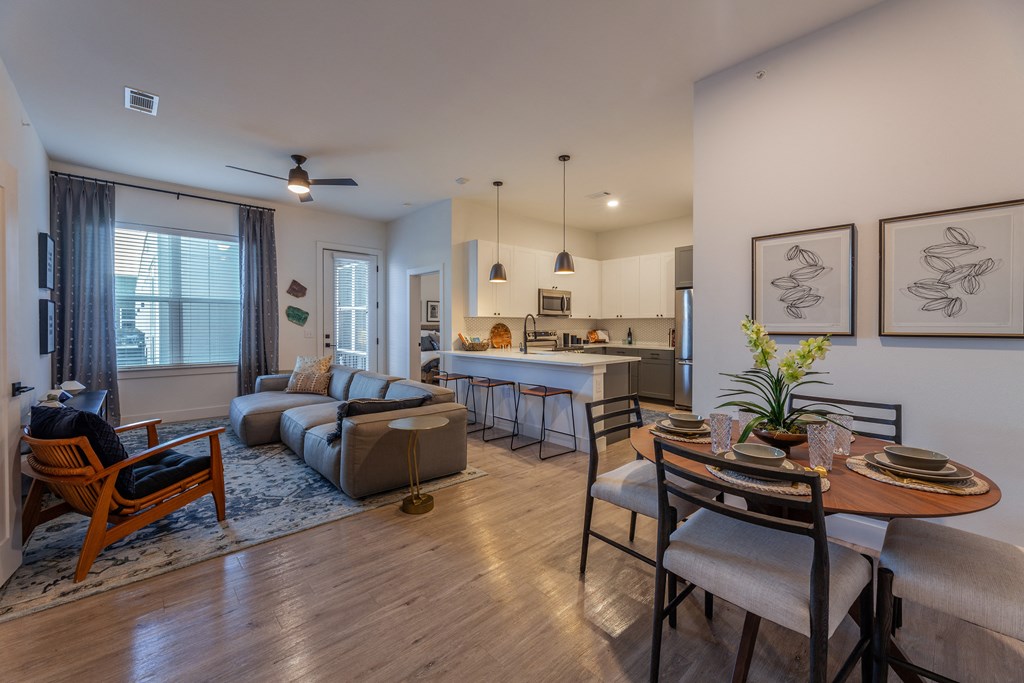 a living and dining area with a table and chairs and a kitchen in the background
