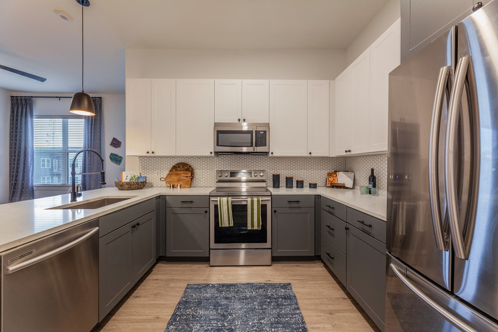 Three-Bedroom Apartments in Old East Dallas, TX - 4600 Ross - Kitchen with Hardwood-Style Flooring, Stainless Steel Appliances, Two-Tone Cabinets, Designer Kitchen Tile Backsplash, and Spacious Quartz Countertops.