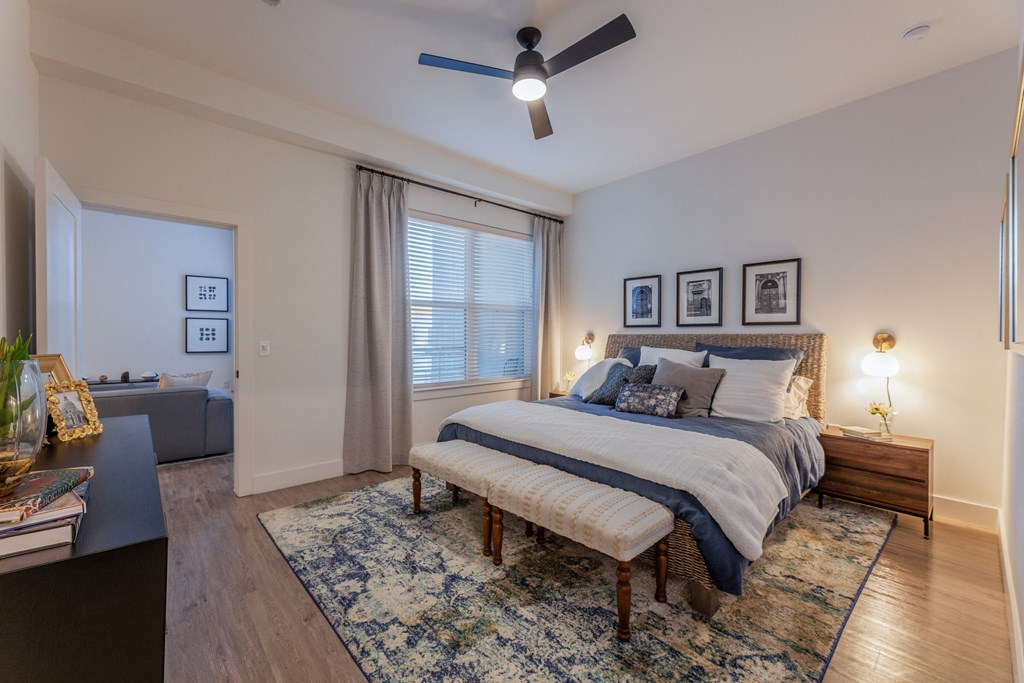 Two-Bedroom Apartments in Old East Dallas, TX - 4600 Ross - Bedroom with Hardwood-Style Flooring, Dresser, Large Bed, Bed Benches, Nightstands with Lamps, Ceiling Fan, and Large Window.