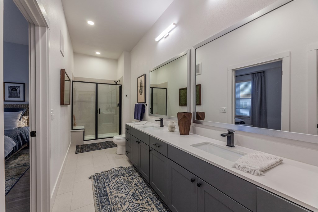 One-Bedroom Apartments in Old East Dallas, TX - 4600 Ross - Bathroom with Dual Sink Vanity, Quartz Countertop, Dual Large Mirrors, Tile Flooring, and Walk-In Shower with Sliding Glass Door.