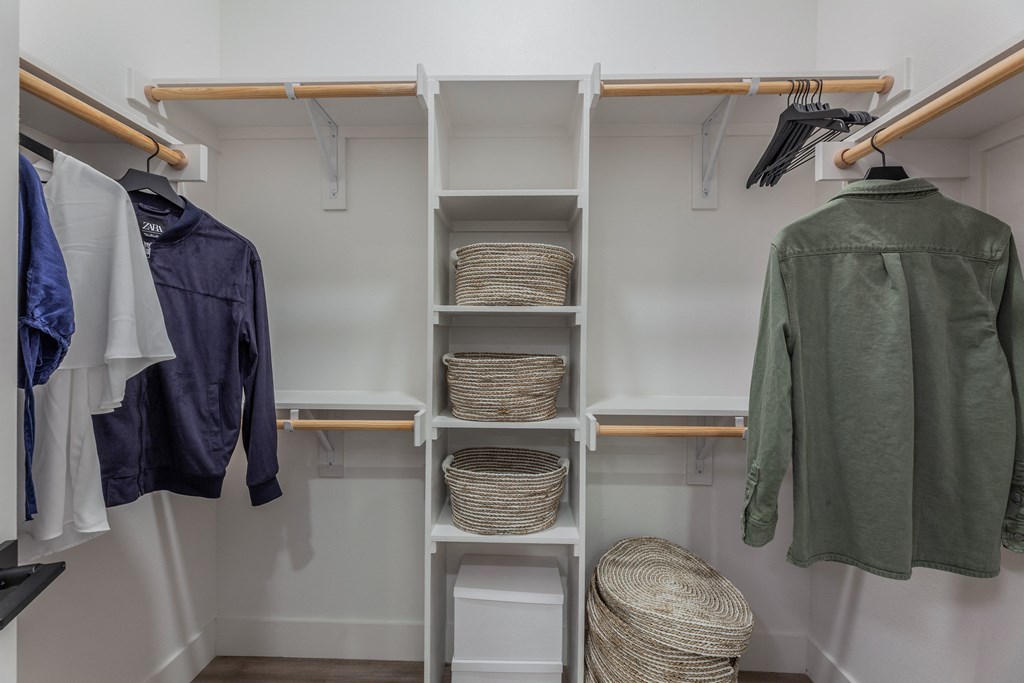 a walk in closet with a white shelving unit and wooden rails