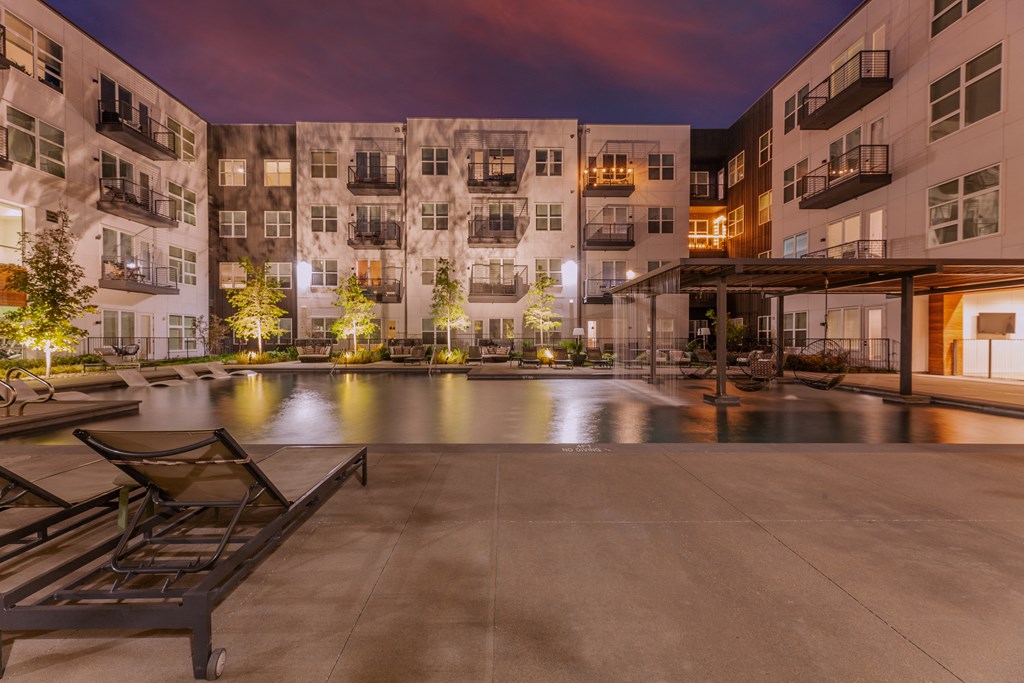Old East Dallas, TX Apartments - 4600 Ross - Oversized Pool with Boho-Inspired Wet Deck, Swings, Cascades, Submerged and Poolside Lounge Seats, and Lighted Trees.