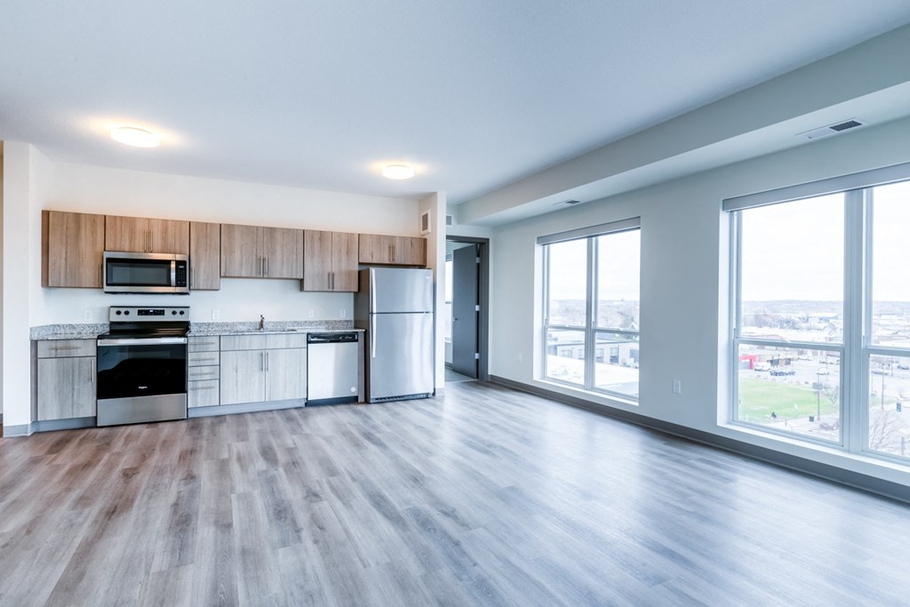 an empty living room with a kitchen and a large window