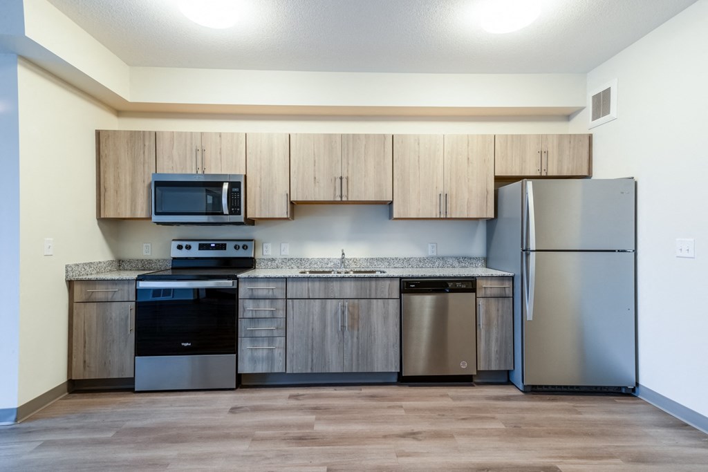 an empty kitchen with stainless steel appliances and wooden cabinets