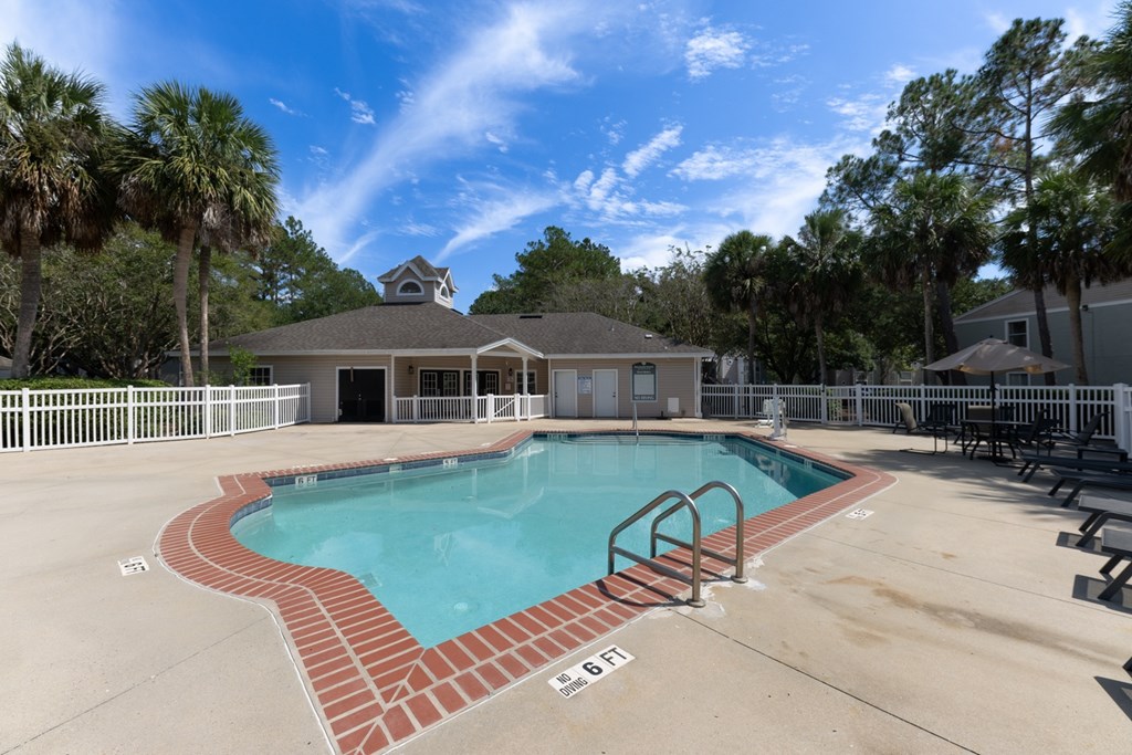 A pool with a brick border and a house in the background.