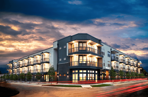 A modern apartment building with a curved facade and balconies is illuminated at dusk.