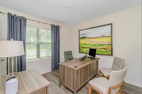 A room with a desk, chair, and a painting on the wall.