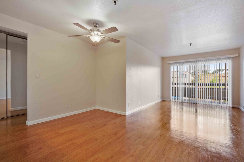 One And Two BR Apartments In Daly City, CA - Serra Commons - Open Living Room With Sliding Glass Door, Ceiling Fan, Wood-Style Flooring, And View Of The Dining Room.