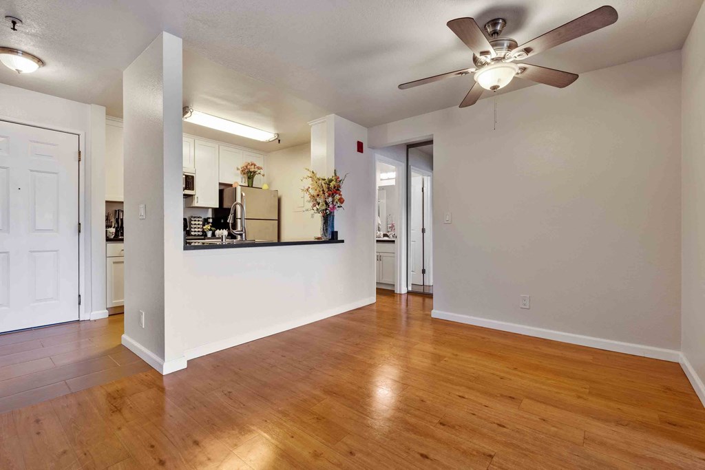 2-Bedroom Apartments In Daly City, CA - Serra Commons - Spacious Living Room With Access To The Kitchen, A Ceiling Fan, And Wood-Inspired Flooring.