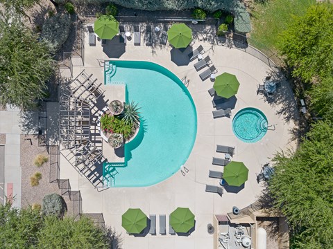 An aerial view of a pool surrounded by green trees and umbrellas.