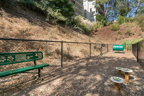 A park with a green bench, a basketball hoop and a green trash bin.