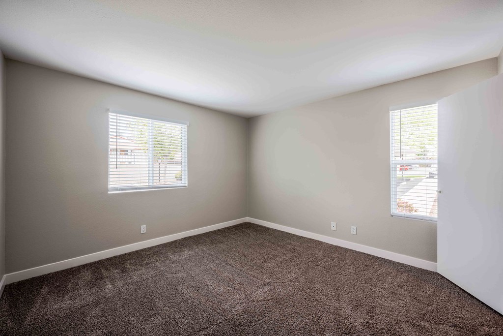 an empty room with carpet and two windows