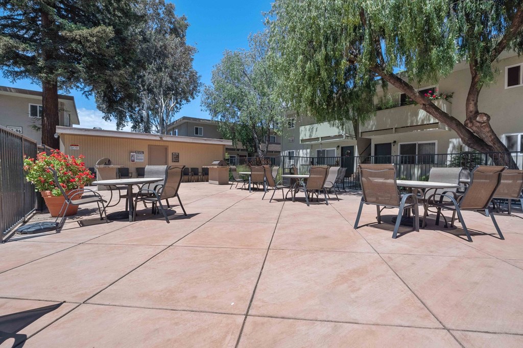 Apartments for Rent in Milpitas, CA - Spring Valley - Gated BBQ Area with Tables, Chairs, Grilling Station, Potted Flowering Plant, and Surrounding Trees.