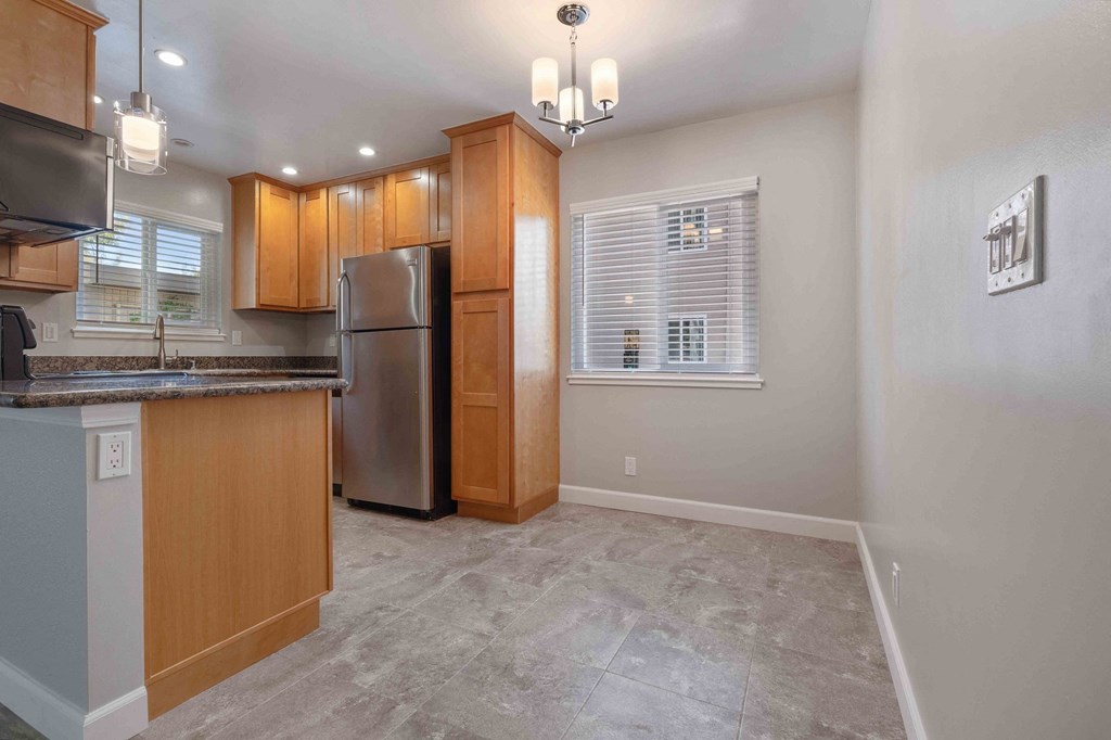 Two-Bedroom Apartments in Milpitas, CA - Spring Valley - Modern Kitchen with Stainless Steel Appliances, Wood-Style Cabinetry, Hanging Lights, Grey Tile Flooring, Granite Countertops, and Large Windows.