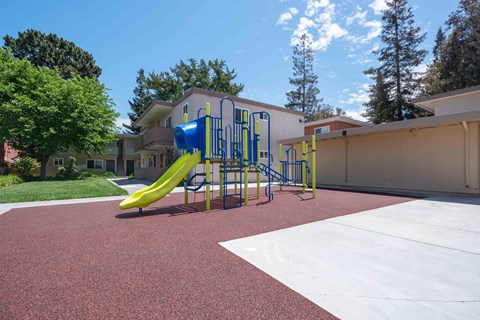 Two-Bedroom Apartments in Milpitas, CA - Spring Valley Apartments - Playground With Blue And Green Slide Structure On Rubber Surface, And Surrounded By Trees.