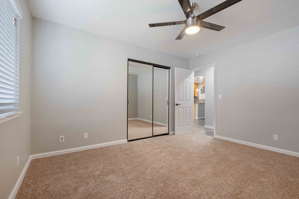 Apartments For Rent In Milpitas, CA - Spring Valley - Roomy Bedroom, Ceiling Fan, Spacious Closet With Mirrors, Carpeted Flooring, and Large Window With Blinds.