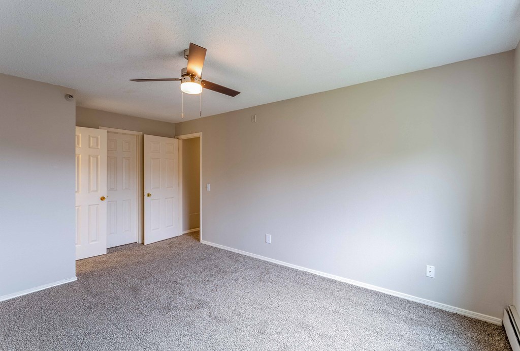 an empty living room with white carpet and a ceiling fan
