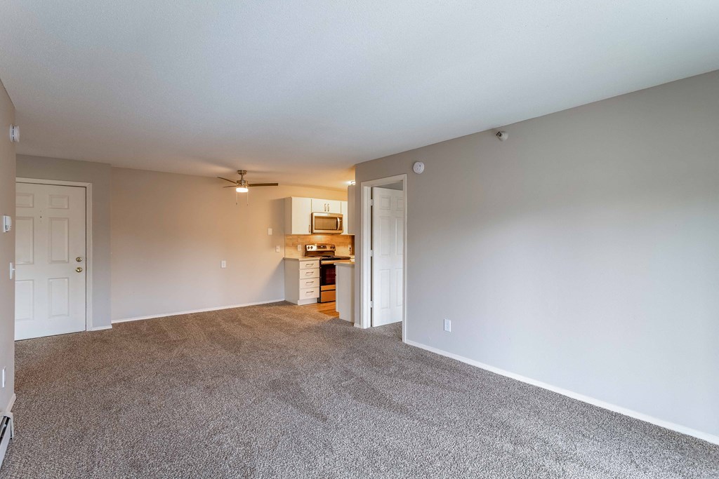 an empty living room with a kitchen in the background