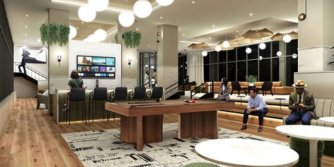 A modern office space with a long wooden table in the center and people sitting and standing around it.