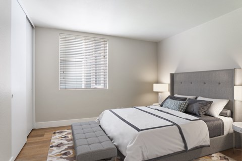 A bedroom with a large bed and a window with blinds.