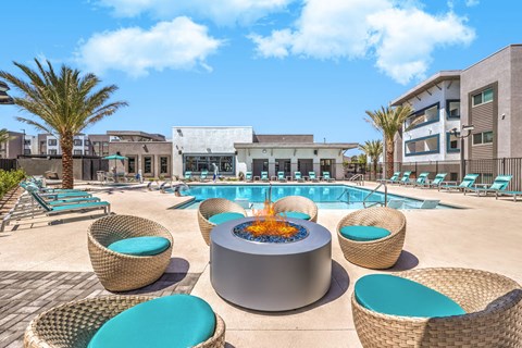 uxurious apartment complex showcasing a stylish outdoor pool area with cozy wicker seating and a modern fire pit, surrounded by palm trees under a clear blue sky.