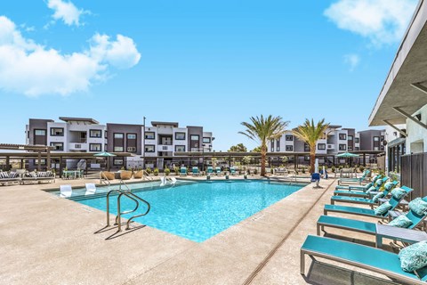 Inviting apartment complex near Las Vegas featuring a sparkling pool, modern architecture, and lush palm trees under a clear blue sky at Summit on Boulder Apartments.