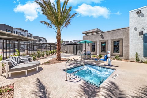 Modern apartment complex with a luxurious outdoor patio, featuring a cozy seating area, vibrant palm tree, and inviting jacuzzi under a clear blue sky at Summit on Boulder Apartments, just 20-minutes from Las Vegas.
