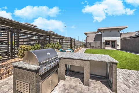 Contemporary outdoor space at Summit on Boulder Apartments with a sleek stainless steel barbecue grill, lush green lawn, and modern seating area under a clear blue sky.