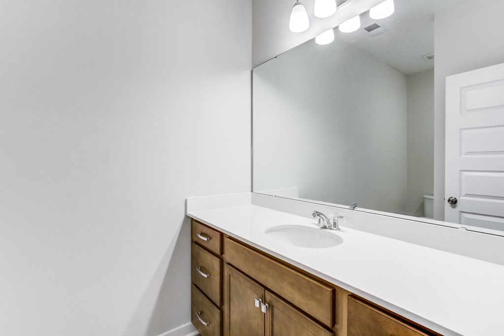 Charleston, SC, Apartments - Sumner Village - Bathroom with Granite Vanity Countertop, Large Mirror, Bright Lights, and Wooden Cabinetry.