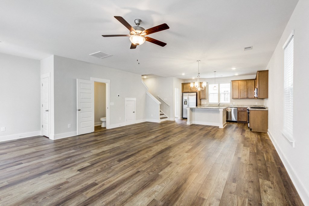 Single Family Homes in North Charleston, SC - Sumner Village - Open-Layout Living Room with Vinyl Plank Flooring, Ceiling Fan, Toilet, Staircase, and View of Kitchen Area.