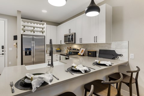 A modern kitchen with a stainless steel refrigerator and wooden chairs.