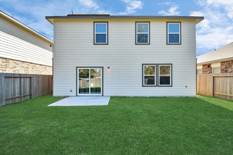 4 Bedroom Single Family Homes for Rent in Houston TX - Imperial Forest - Back of a Home Exterior, with White Walls, Windows, Sliding Glass Back Door, and Grassy Lawns in a Fenced-In Yard