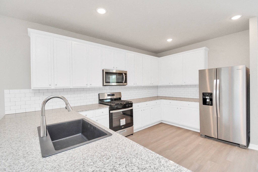 Three-BR Homes for Rent in Katy, TX - Villas at Sunterra - Kitchen with White Cabinets, Stainless Steel Appliances, Granite Countertops, and Wood-Style Flooring