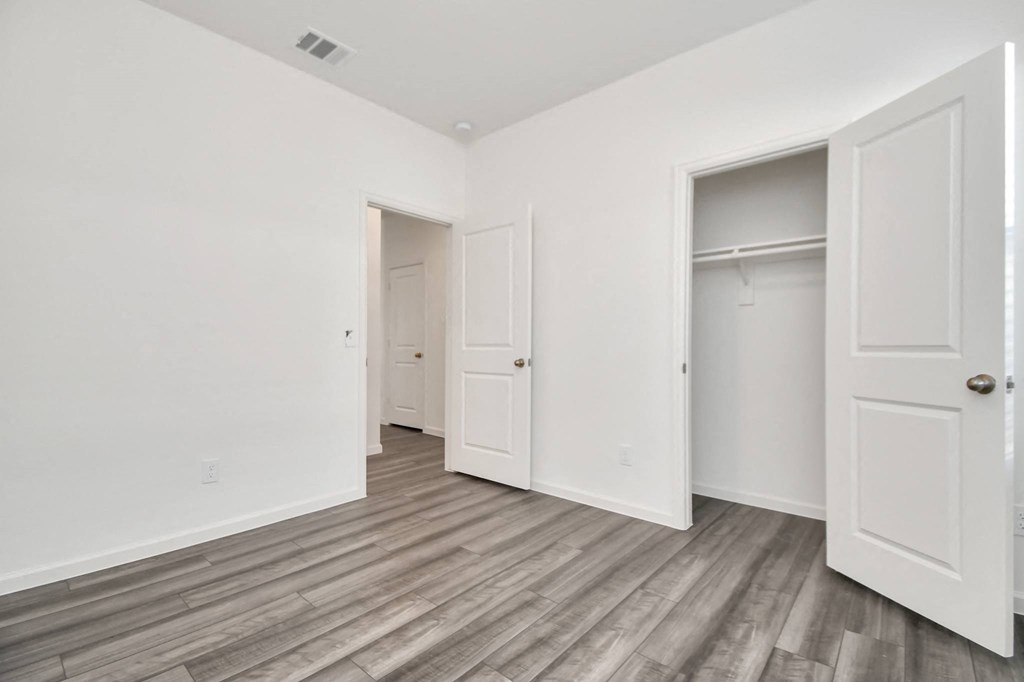 A room with white walls and wood flooring with three doors.