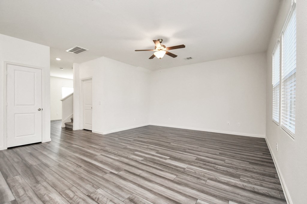 Five Bedroom Single Family Homes for Rent in Houston TX - Imperial Forest - Unfurnished Living Room Space with Wood-Style Flooring, White Walls, a Ceiling Fan, Closet Doors, a Window, and View of the 