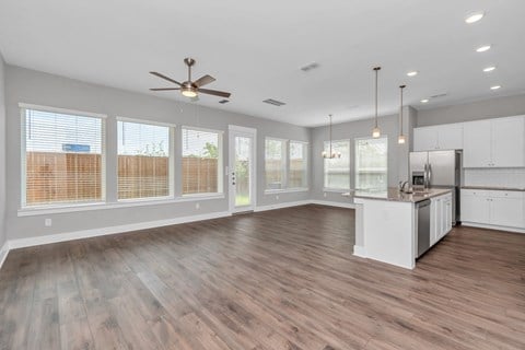 an empty living room with a kitchen and a ceiling fan