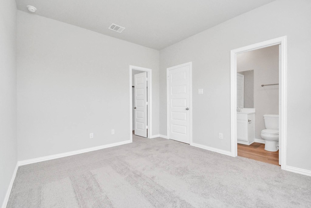 a bedroom with two doors and a bathroom in the background