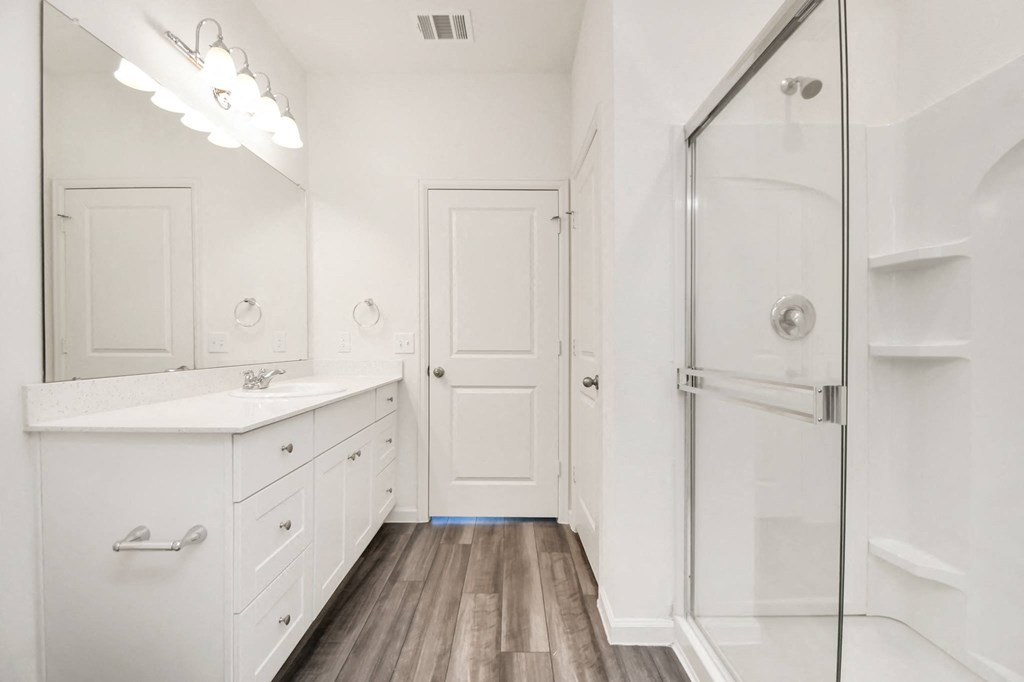 3 Bedroom Homes for Rent in Houston TX - Imperial Forest - Bright, White-Walled Bathroom with a Glass Shower, White Cabinetry, Mirror, and Wood-Style Flooring