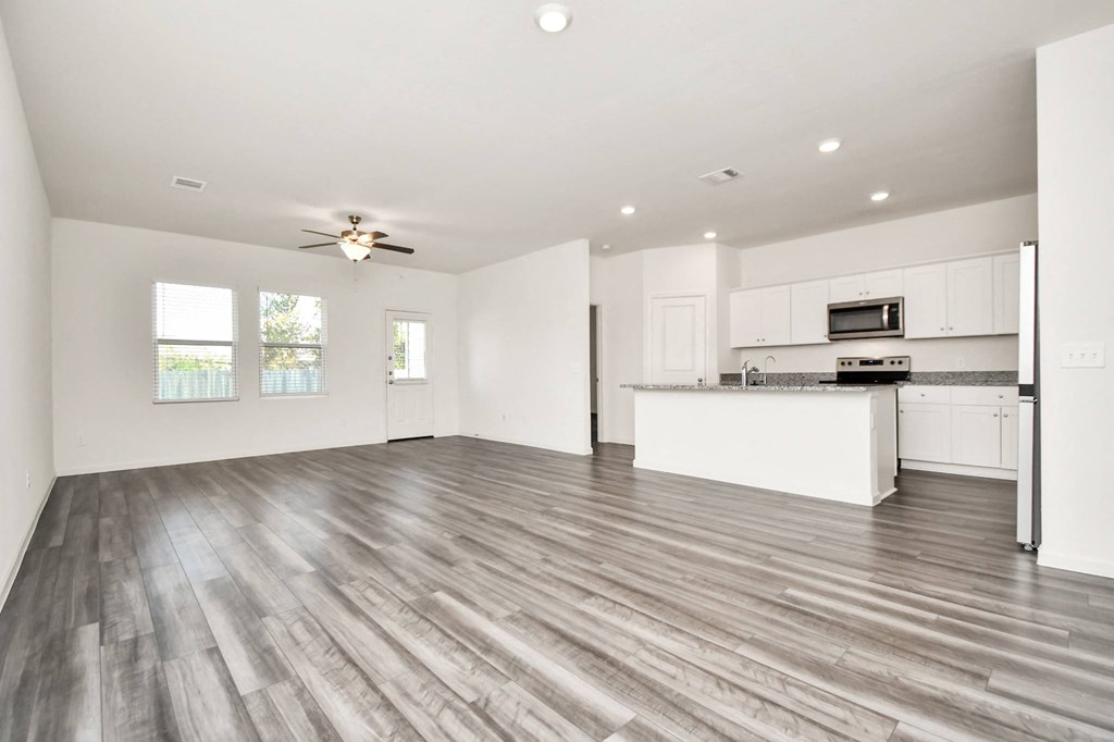 A spacious kitchen and living room with wood flooring and white walls.