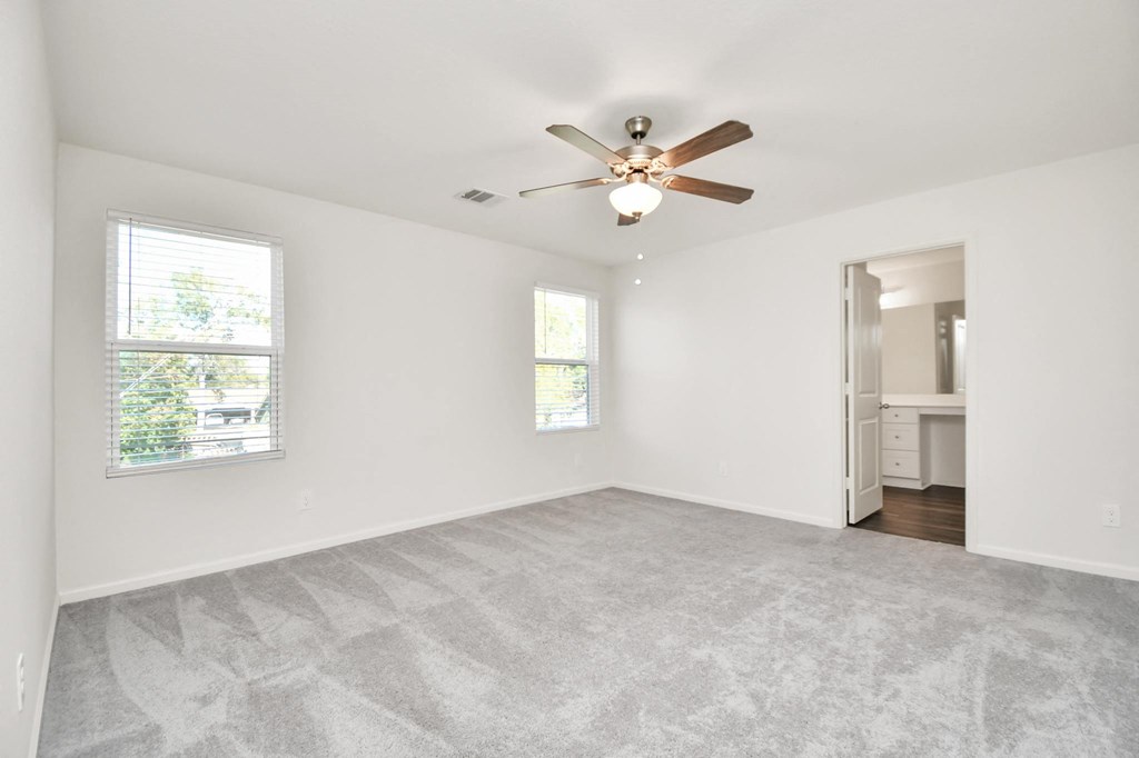 A room with a ceiling fan and two windows.