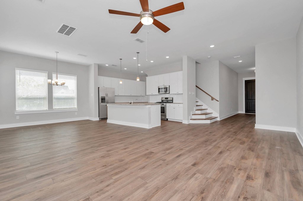Dog-Friendly homes for rent in Heights, Houston TX - The Crossing at Timbergrove - Open-Concept, Empty Living Space with Hanging Lights, a Ceiling Fan, Windows, Hardwood-Inspired Flooring, and a View 