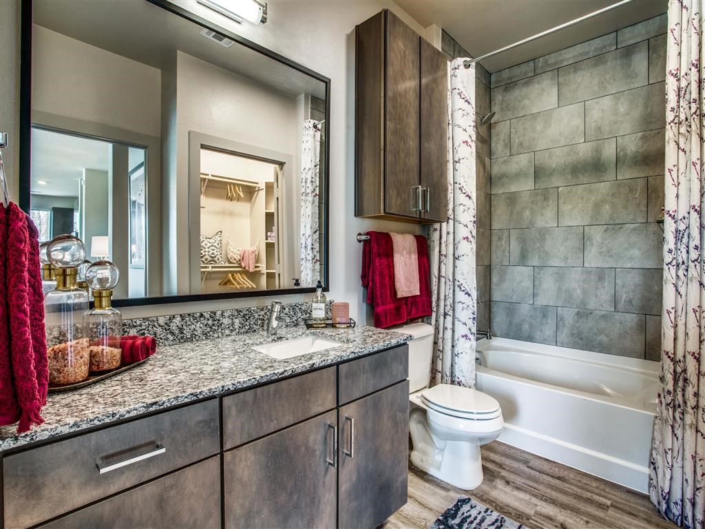 Dog Friendly Apartments In Grand Prairie, TX - Waters Edge At Mansfield - Bathroom With Ceramic Tub And Shower, Modern Decor, Gray Cabinets, Granite Countertops, And Wood Style Flooring