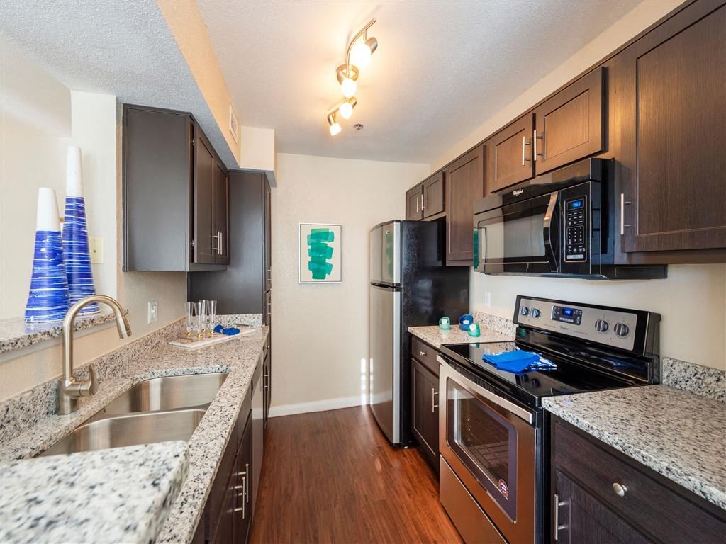 Two BR Apartments in League City, TX - Anchor at South Shore - Kitchen with Granite Countertops, Dark Wood Cabinetry, Stainless Steel Appliances, Wood-Style Flooring, and Ceiling Light Fixtures
