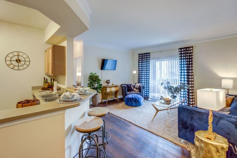 Two-Bedroom Apartments in San Antonio, TX - Club at Stone Oak - Living Room with Wood-Style Flooring, a Couch, Chair, Coffee Table, End Tables with Lamps, TV, and Sliding Glass Door