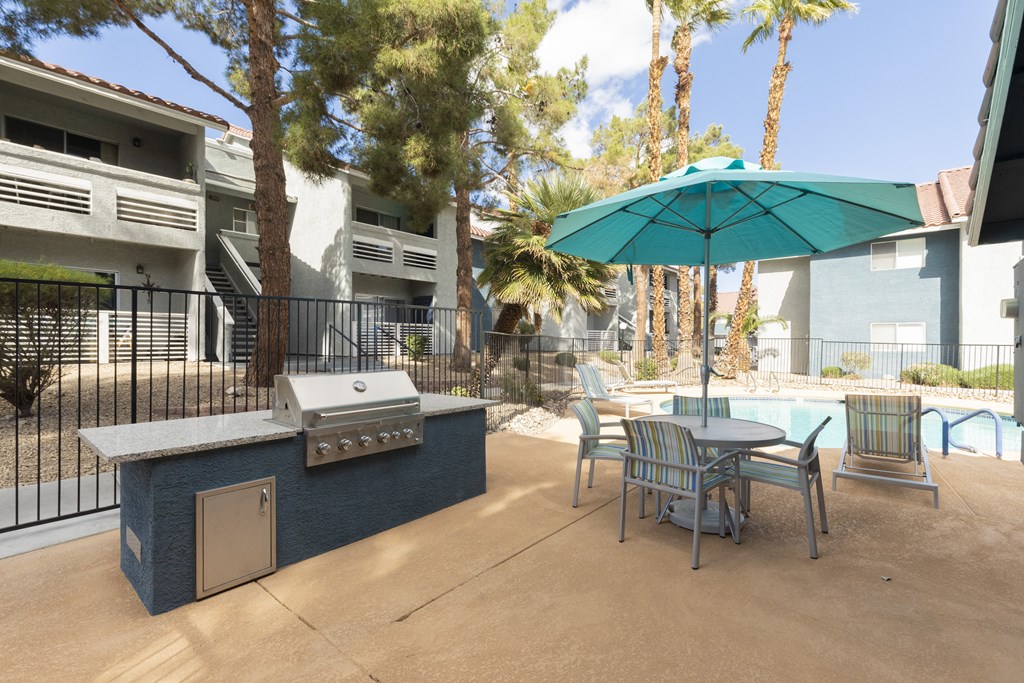 a patio with a grill and a table with chairs and an umbrella